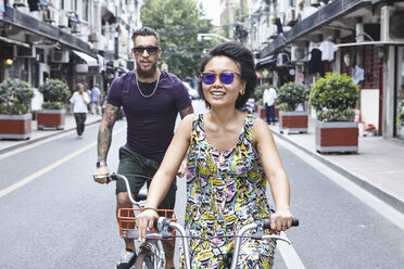 Multiethnisches Hipster-Paar, das mit dem Fahrrad durch die Stadt fährt, Shanghai French Concession, Shanghai, China - CUF10103