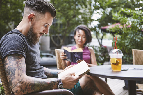 Multiethnisches Hipster-Paar liest Bücher in einem Straßencafé, Shanghai French Concession, Shanghai, China - CUF10109