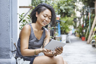 Frau sitzt auf der Türschwelle in einer Wohnstraße und schaut auf ein digitales Tablet, Shanghai French Concession, Shanghai, China - CUF10123