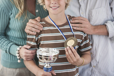 Beschnittene Ansicht eines Jungen, der stolz eine Trophäe und eine Medaille hält - CUF10140