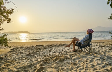 Woman on beach in deckchair looking away at sea, Florianopolis, Santa Catarina, Brazil, South America - CUF10167