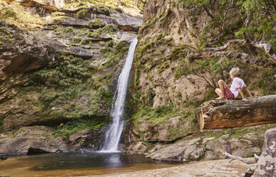 Junge sitzt auf einem Baumstamm und betrachtet einen Wasserfall, Samaipata, Santa Cruz, Bolivien, Südamerika - CUF10176