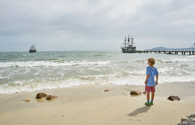 Boy on beach looking away at ships on sea, Florianopolis, Santa Catarina, Brazil, South America - CUF10185