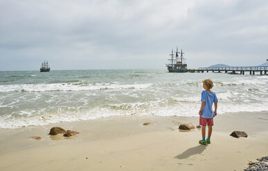 Junge am Strand mit Blick auf Schiffe auf dem Meer, Florianopolis, Santa Catarina, Brasilien, Südamerika - CUF10185