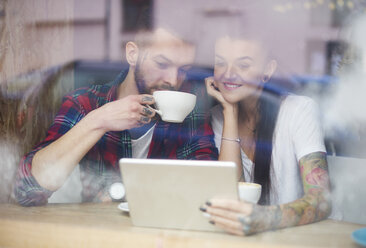 Blick durch ein Fenster auf ein Paar in einem Café, das ein digitales Tablet benutzt - CUF10211