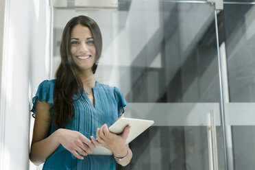 Window view portrait of young businesswoman with digital tablet at office entrance - CUF10227