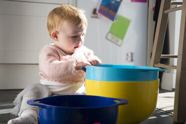 Baby girl sitting on kitchen floor playing with bowls - CUF10240