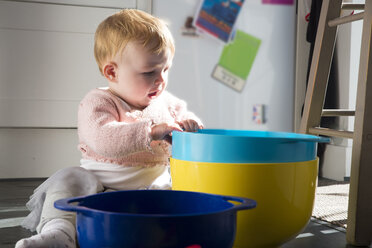 Kleines Mädchen sitzt auf dem Küchenboden und spielt mit Schüsseln - CUF10240