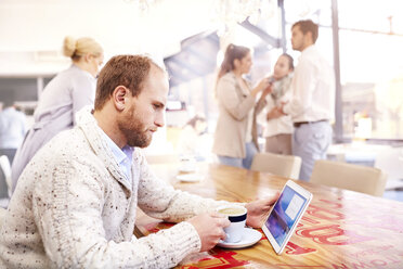 Junger Mann allein in einem Café mit Blick auf ein digitales Tablet - CUF10252