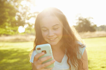 Mädchen schaut im sonnenbeschienenen Park auf ihr Smartphone - CUF10340