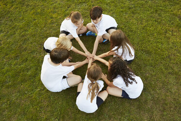 Overhead view of boy and girl sport team sitting on grass in circle on playing field - CUF10342