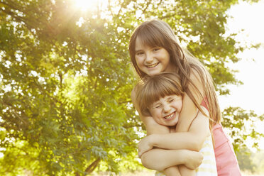 Portrait of girl being hugged by big sister in park - CUF10348