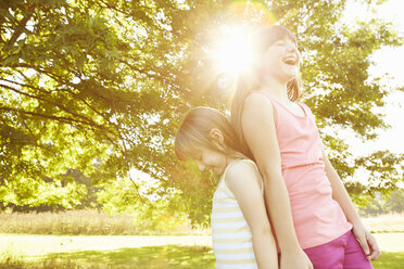 Girl and big sister back to back in park - CUF10349