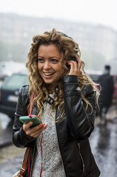 Woman in street listening to music through headphones - CUF10399