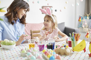 Girl and mother painting easter eggs at table - CUF10403