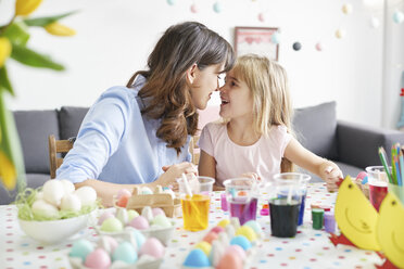 Woman and daughter nose to nose while painting easter eggs at table - CUF10404