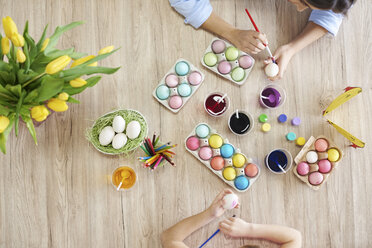 Overhead view of woman and daughter's hands painting easter eggs at table - CUF10405