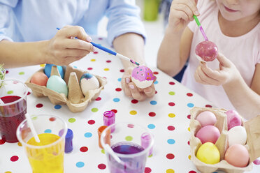 Cropped shot of woman and daughter's hands painting easter eggs at table - CUF10406