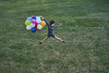 Glückliche junge Frau mit einem Bündel Luftballons, die auf einer Wiese in die Luft springen - BEF00081