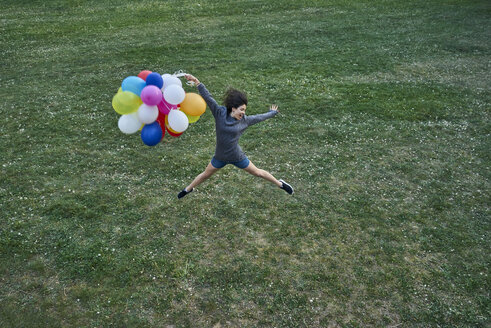 Glückliche junge Frau mit einem Bündel Luftballons, die auf einer Wiese in die Luft springen - BEF00081