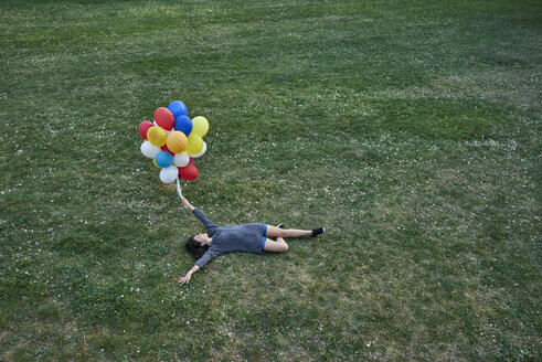 Junge Frau mit einem Strauß Luftballons auf einer Wiese liegend - BEF00082