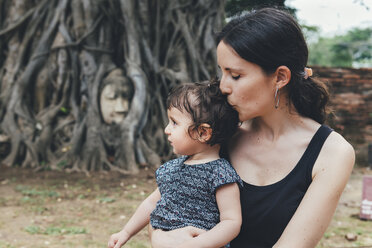 Mother kissing her daughter in Wat Mahathat Ayutthaya with buddha head in tree roots in the background - GEMF01989