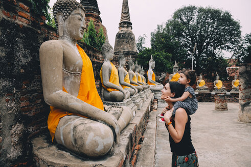 Thailand, Bangkok, Ayutthaya, Buddha statues in a row in Wat Yai Chai Mongkhon, mother and daughter in front of a buddha statue - GEMF01993