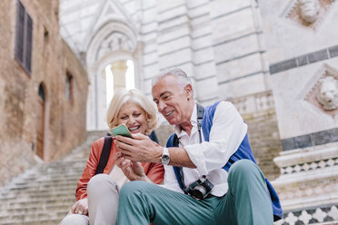 Touristenpaar, das auf der Treppe des Doms von Siena sein Smartphone betrachtet, Toskana, Italien - CUF10423