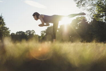 Mature woman in park, balancing on one leg, in yoga position, low angle view - CUF10465