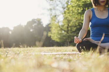 Mature woman in park, sitting in yoga position, low angle view - CUF10467