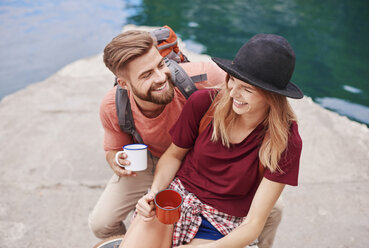 Couple by water holding enamel mugs smiling, Krakow, Malopolskie, Poland, Europe - CUF10518