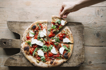 Woman taking pizza slice from pizza on chopping board, overhead view - CUF10530