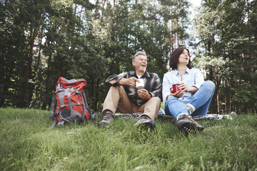 Älteres Paar, das sich im Gras ausruht, mit Zinnbechern in der Hand, daneben ein Rucksack - CUF10538
