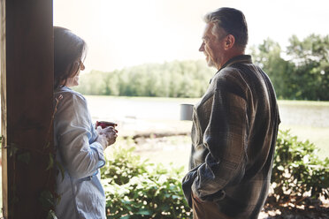 Mature couple standing on veranda, holding tin cups, smiling - CUF10544