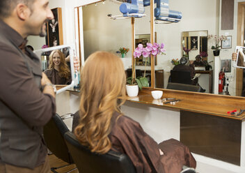 Friseurin zeigt Kunden gestylte lange rote Haare im Salon - CUF10561