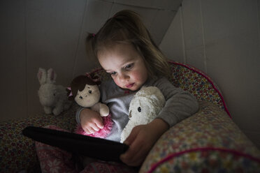 Female toddler sitting up in bed staring at digital tablet - CUF10566