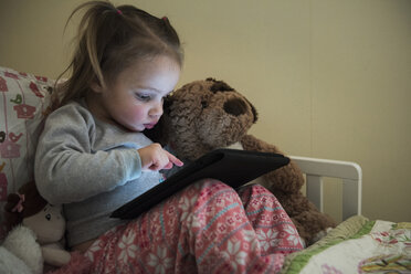 Female toddler sitting up in bed using touchscreen on digital tablet - CUF10567