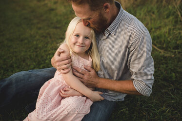 Daughter sitting on fathers lap on grass - CUF10572