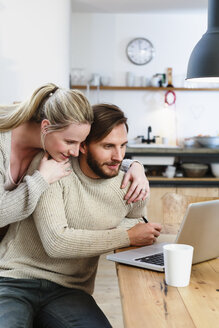 Mid adult couple looking at laptop in kitchen - CUF10578