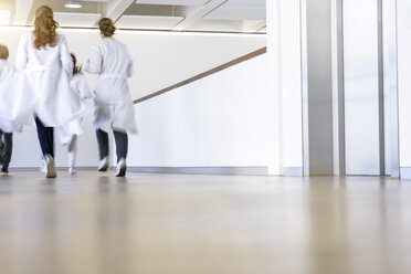 Rückansicht von männlichen und weiblichen Ärzten, die in einem Krankenhauskorridor laufen - CUF10588