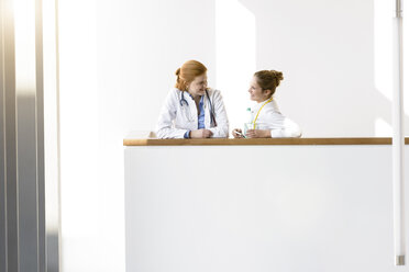 Two young female doctors leaning against hospital balcony talking - CUF10596