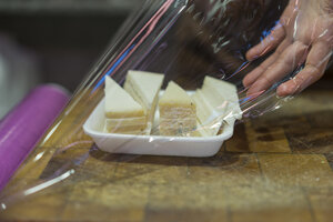 Verkäuferin verpackt Käse in Schale mit Frischhaltefolie - AFVF00457