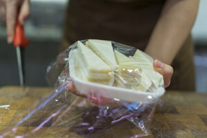 Verkäuferin verpackt Käse in Schale mit Frischhaltefolie - AFVF00458