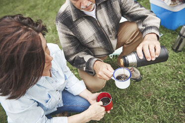 Mature couple crouching on grass, man pouring hot drink from drinks flask, elevated view - CUF10648