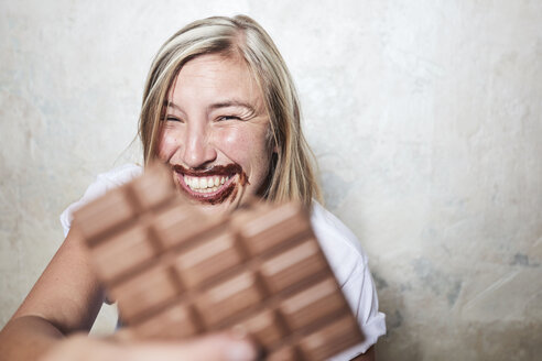 Porträt einer Frau, die eine Tafel Schokolade isst, Schokolade um den Mund - CUF10679