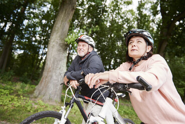 Mature couple walking along rural pathway with bicycles, looking at view - CUF10682