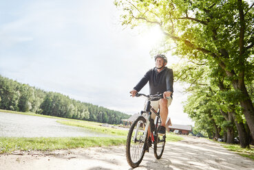 Senior man cycling beside lake - CUF10683