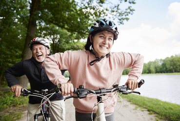 Mature couple cycling beside lake, laughing - CUF10684