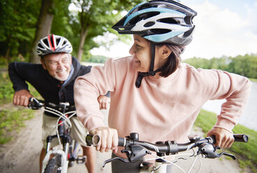 Mature couple cycling beside lake, laughing - CUF10685