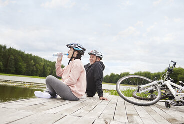 Mature couple relaxing on jetty, bicycles beside them - CUF10687